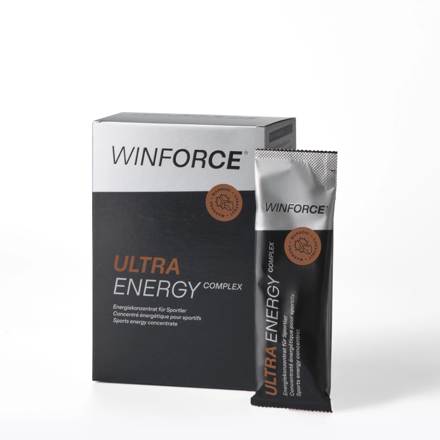 Detailaufnahme der WINFORCE ULTRA ENERGY COMPLEX Marroni Energiekonzentrat-Verpackung. Eine dunkelgraue Box steht neben einem silbernen Sachet, beide mit dem orangefarbenen Schriftzug "ULTRA ENERGY" und einem braunen Marroni-Logo, das die Geschmacksrichtung Kastanie für Sportler hervorhebt.